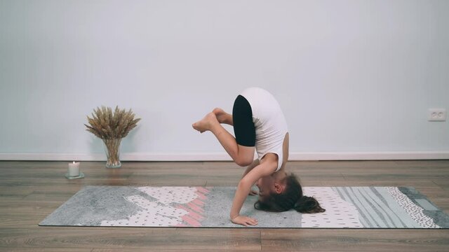 Caucasian girl does yoga in front of a laptop Child does a headstand Girl does gymnastic exercises Gymnastics Online Yoga at home
