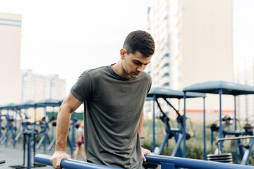 Fototapeta na wymiar Young handsome man doing push-ups on the uneven bars outdoor. Sports, fitness, gymnastics workout