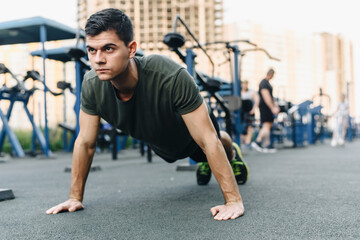 Fototapeta na wymiar A young man does push-ups on the street on a specialized sports ground with trainers. Build muscles in the fresh air. Sport and healthy lifestyle concept