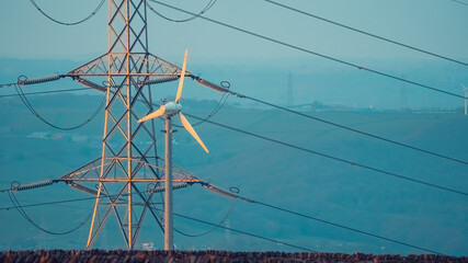 Small wind turbine in front of an electricity pylon - obrazy, fototapety, plakaty