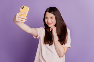 Photo of cheerful adorable young woman hold mobile phone make selfie posing on purple wall