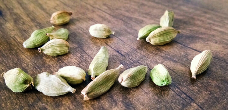 Closeup top view of dried green Elettaria cardamomum fruits with seeds, cardamom spice scattered on wooden background