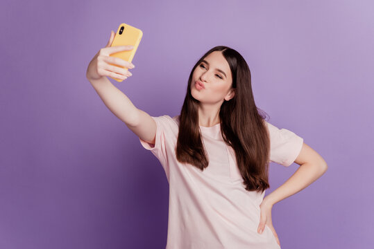 Photo of cheerful cute young woman hold cellphone take selfie send air kiss