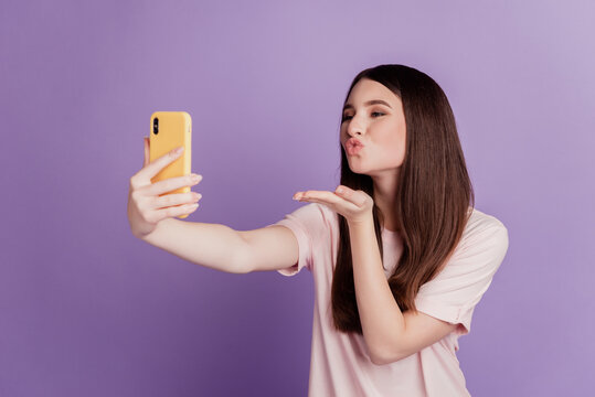 Photo of cheerful cute young woman hold smartphone take selfie hold palm blow air kiss