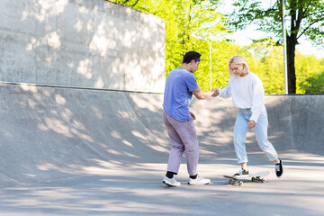  Carefree teenage couple in a skate-park. Guy giving a lesson of skateboarding for his girlfriend.