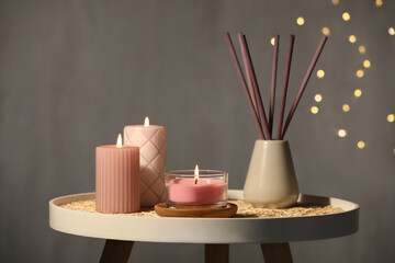 Burning candles and reed diffuser on table against grey background - obrazy, fototapety, plakaty