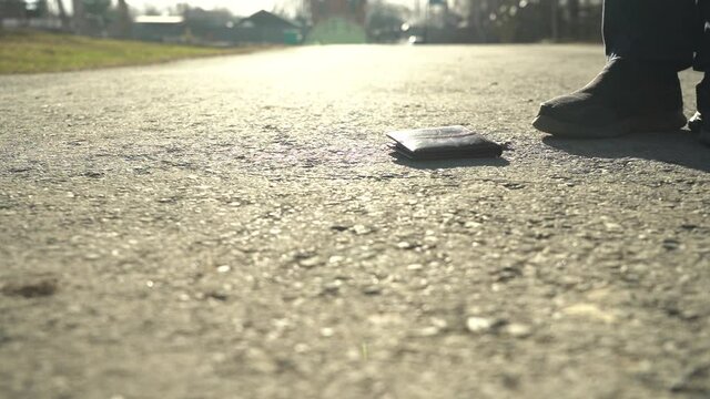 The man picks up the wallet from the sidewalk. The concept of carelessness and loss of money