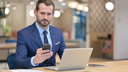 Middle Aged Businessman using Smartphone and Laptop in Office 