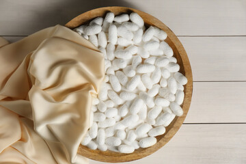 Cocoons with bowl and silk fabric on white wooden table, flat lay