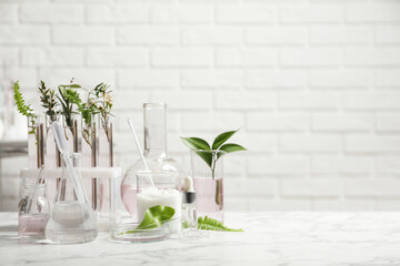 Organic cosmetic products, natural ingredients and laboratory glassware on white marble table, space for text