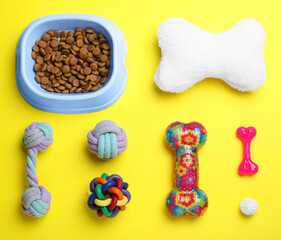 Feeding bowl and toys for pet on yellow background, flat lay