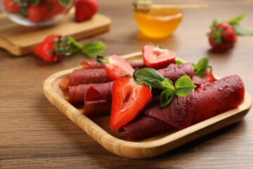 Delicious fruit leather rolls and strawberries on wooden table, closeup