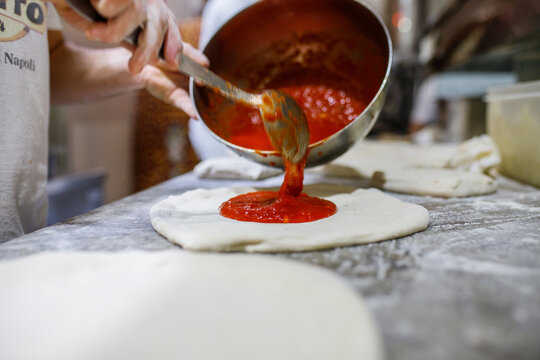 Pizzaiolo mentre mette del sugo di pomodoro su un disco di pizza napoletana crudo 