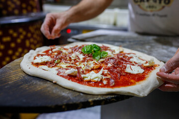 Pizzaiolo mentre sistema una pizza napoletana pronta da infornare con mozzarella, salame piccante,...