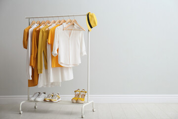 Rack with bright stylish clothes, hat and shoes near light grey wall indoors, space for text