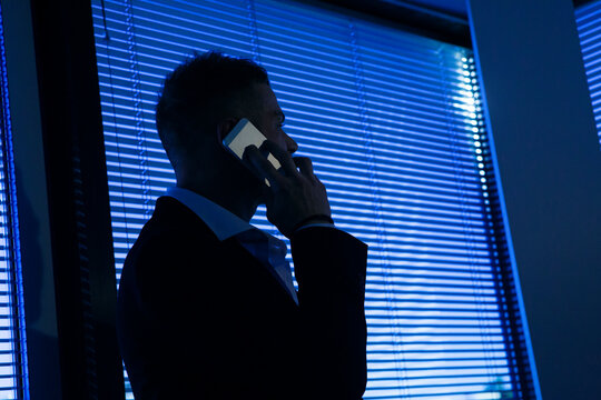 Uomo bianco biondo con tatuaggi vestito in giacca e camicia fa una chiamata dal cellulare in piedi  nel suo ufficio 