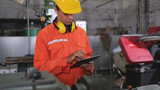 Factory worker man or technician use tablet to inspect and check function of machine in workplace while her co-worker woman is working in the background.