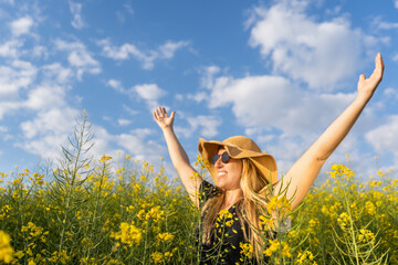 Happy woman enjoying summer raising arms in yellow flowers ,rapeseed field at sunset.Spring concept.