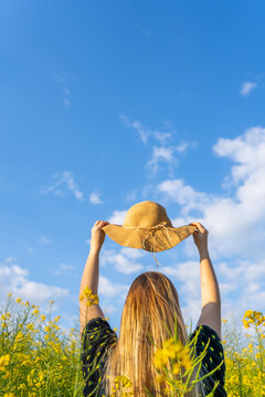 Woman holding sun hat in yellow flowers field at sunset.Happy female in spring sunny day concept lifestyle.Vertical photography with copy space.