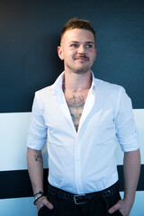 Uomo bianco biondo con tatuaggi  e camicia bianca guarda serio isolato su sfondo neutro