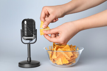 Woman making ASMR sounds with microphone and nacho chip on grey background, closeup