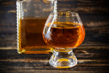 Wineglass with cognac and glass flacon on wooden plank surface, close-up.