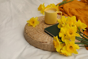 Bouquet of beautiful daffodils, book and coffee on bed, space for text