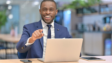 African Businessman with Laptop Pointing at the Camera 