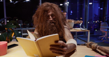 In modern office savage caveman reading a journal screaming and yelling having fun pretending to...