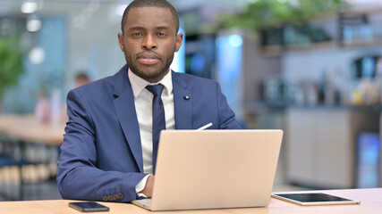 African Businessman with Laptop Looking at Camera in Cafe 