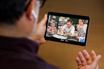 Fototapeta na wymiar Dettaglio di un computer portatile nel cui schermo compaiono tre persone che preparano un dolce in cucina da remoto, in videoconferenza con un uomo seduto davanti al computer