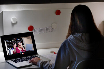 Dettaglio di un computer portatile nel cui schermo compare una signora che saluta da remoto in...