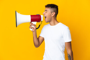 Young brazilian man isolated on yellow background shouting through a megaphone to announce...