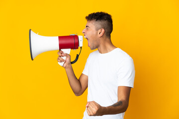 Young brazilian man isolated on yellow background shouting through a megaphone to announce...