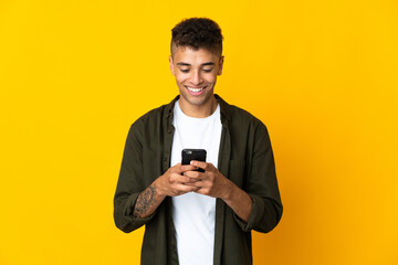 Young brazilian man isolated on yellow background sending a message or email with the mobile
