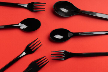 Forks, Spoons and Knives on red background. Plastic cutlery, ecology, environmental pollution by plastic, disposable tableware, waste recycling concept. Pattern, flat lay
