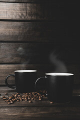 two cups of hot coffee with steam and coffee beans on a wooden and black background. hot drink.
