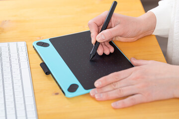 Close-up of female hands using digital graphics tablet and stylus while working in modern office
