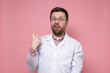Puzzled doctor in glasses and a white coat points up with index finger and makes a silly grimace. Pink background.