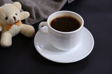 Black coffee and a teddy white bear on a black background.