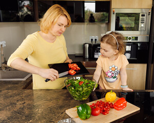 Happy mom and daughter little girl are happy to spend time together cooking fresh vegetable salad. Concept of healthy eating, accustoming children to work