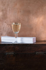 Retro still life with a glass of white wine on a copper background. Stack of invitation cards on an old chest. Vertical image. Copy space. 
