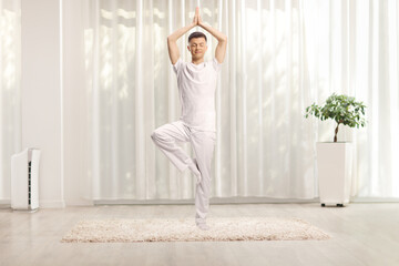 Guy in white clothes standing practicing yoga in a living room