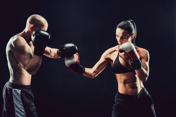 Shirtless Woman exercising with trainer at boxing and self defen