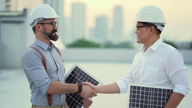 Solar Power Plant Engineer Meeting With Asian Business Man And Handshake Close Deal To  Install Solar Panels On Rooftop Of Factory In Morning Or Sunset . Shaking Hands Agreement To Solar Power Energy