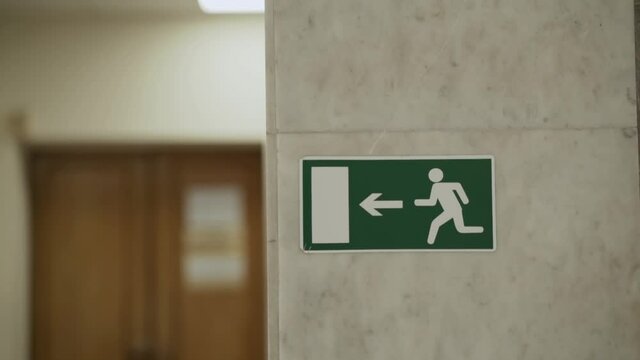 Green sign indicating direction of the emergency exit is attached to the granite pole in the room