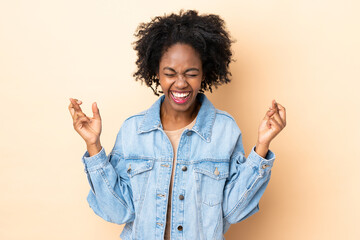 Young African American woman isolated on beige background with fingers crossing