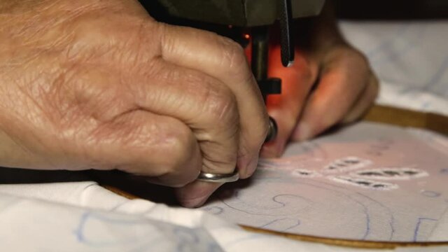 An old woman makes embroidery on an old sewing machine