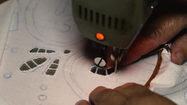 The hands of an elderly woman who is working on an embroidery machine
