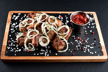 Grilled meat skewers, kebab with onion and sauce on a plate of dark stone and wooden sides sprinkled with salt and spices